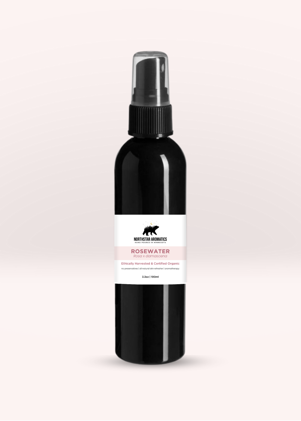 Black plastic spray bottle of rosewater hydrosol by Northstar Aromatics on soft light pink background