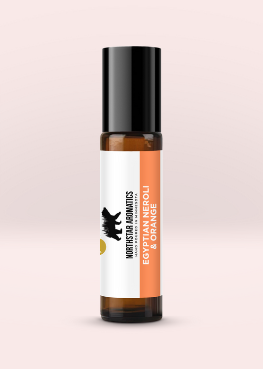 Egyptian Neroli & Orange Roll-On essential oil blend in amber glass bottle with black cap on pink background.