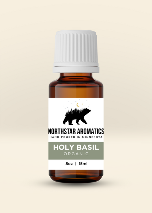 Amber glass bottle of organic Holy Basil essential oil by Northstar Aromatics with white ribbed cap on light beige background