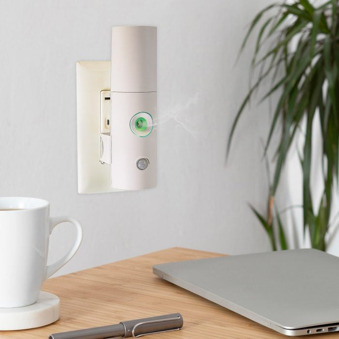 Cool Mist Plug In Waterless Diffuser plugged in on wall releasing mist beside laptop and coffee cup on desk.