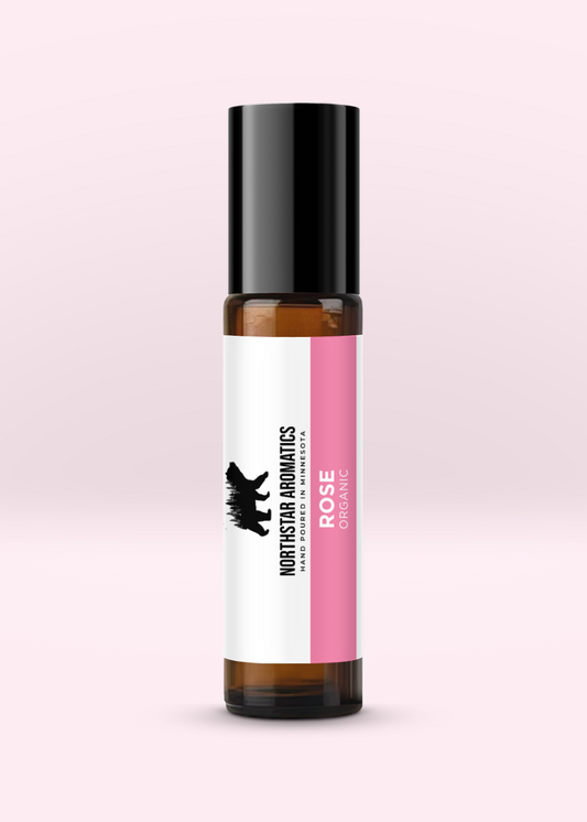 Amber glass roll-on bottle of organic Rose essential oil by Northstar Aromatics with black cap on pale pink background