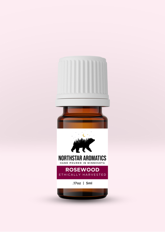 Amber glass bottle of ethically harvested Rosewood essential oil by Northstar Aromatics with white ribbed cap on pale pink background