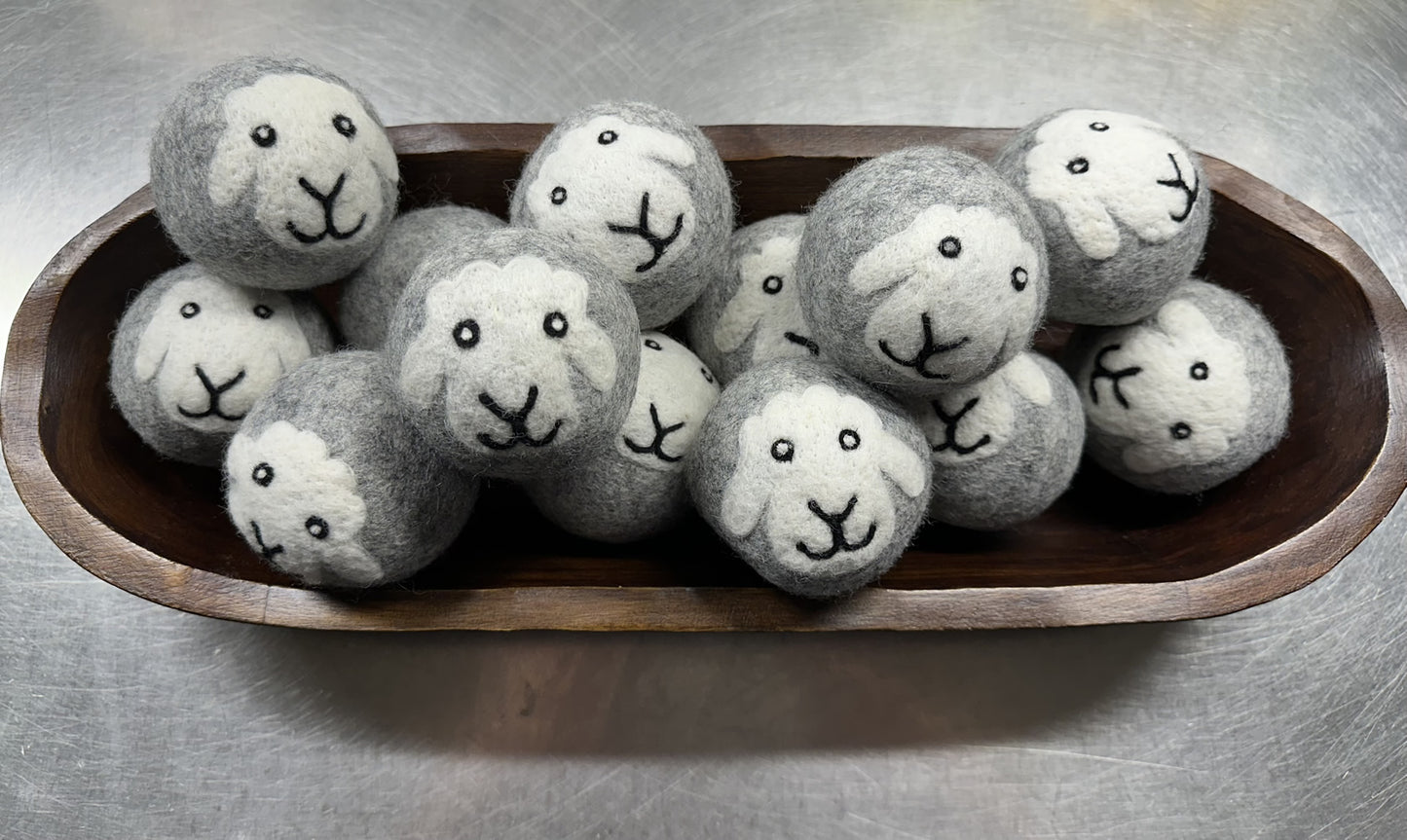 Laundry Balls made of handmade New Zealand wool with cute sheep faces in a wooden bowl for eco-friendly drying.