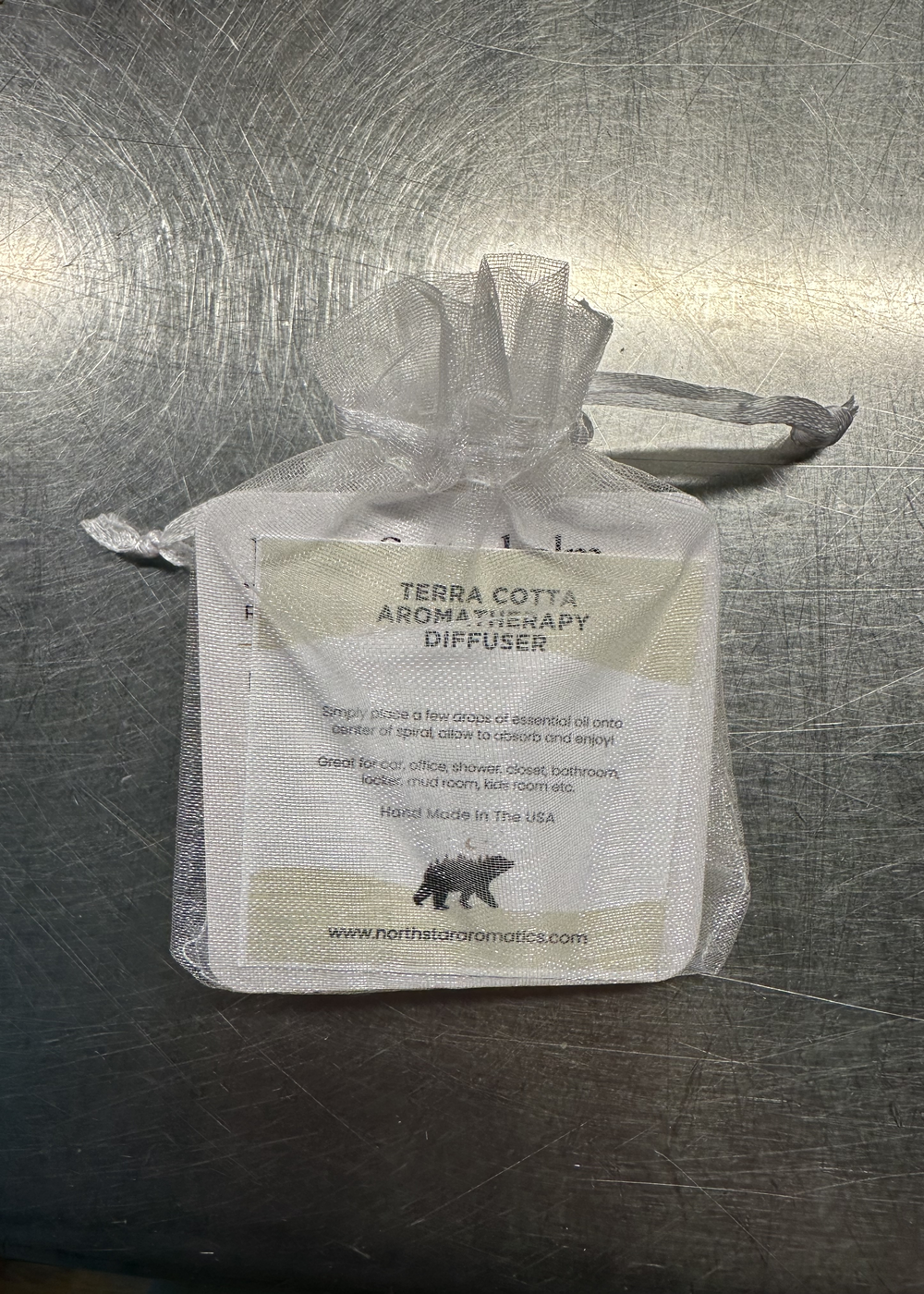 Terra Cotta Aromatherapy Diffuser in a white mesh pouch with product instructions on a metallic surface.